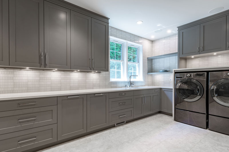 Laundry room with gray cabinets and tile backsplash.
